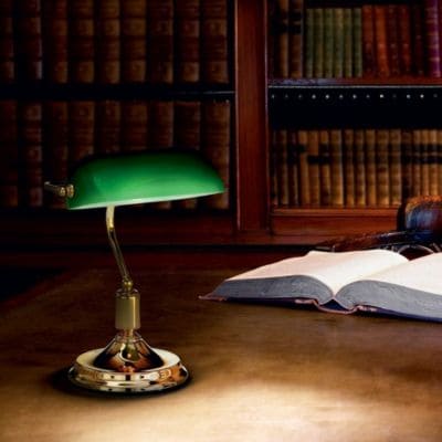 Pièce de type bibliothèque avec un livre ouvert devant lequel apparaît la lampe verte Lawyer de la marque Ideal Lux.