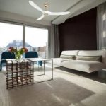 Salon lumineux avec canapé blanc et table basse en métal, ventilateur moderne au plafond et lumière naturelle abondante. meilleur destratificateur maison