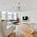 Lustre élégant à lustres argentés suspendu au plafond, dans un salon lumineux avec canapé vert, fauteuils blancs et sol en bois.