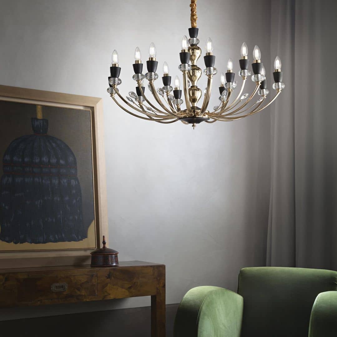 Grand lustre antique à bougies doré suspendu au-dessus d’un salon avec canapé vert et peinture encadrée sur un mur gris.