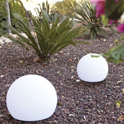 Deux boules lumineuses blanches posées sur des graviers dans un jardin.