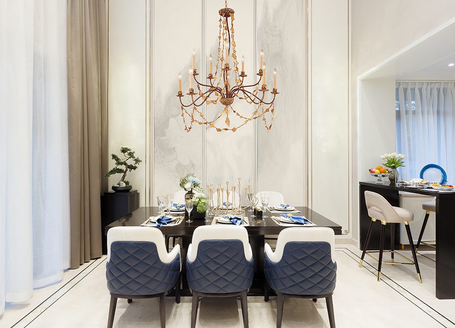 Salle à manger élégante avec une grande table noire et des chaises capitonnées bleu gris sous un chandelier ancien.