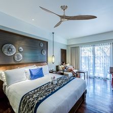 Ventilateur de plafond suspendu au centre d'une chambre moderne avec lit à baldaquin et grande baie vitrée.