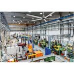 Vue d’un grand atelier industriel avec des machines et équipements disposés en rangées et un sol éclairé.