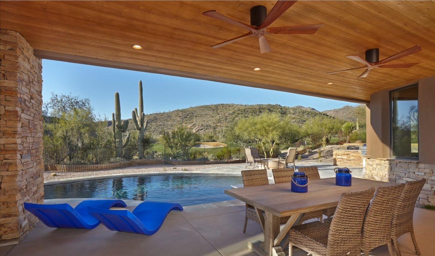 Vue d’une terrasse extérieure abritée avec deux ventilateurs de plafond, table et chaises en rotin, et une piscine à